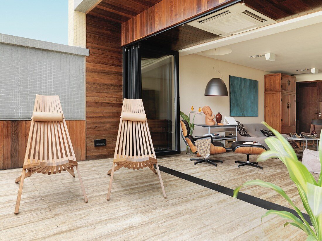 Outdoorstühle aus Holzlamellen auf Terrasse mit Steinboden und Blick in offenen Wohnraum