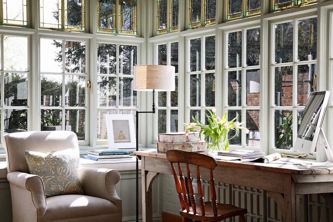 Simple desk and comfortable armchair in fully glazed bay with lattice windows