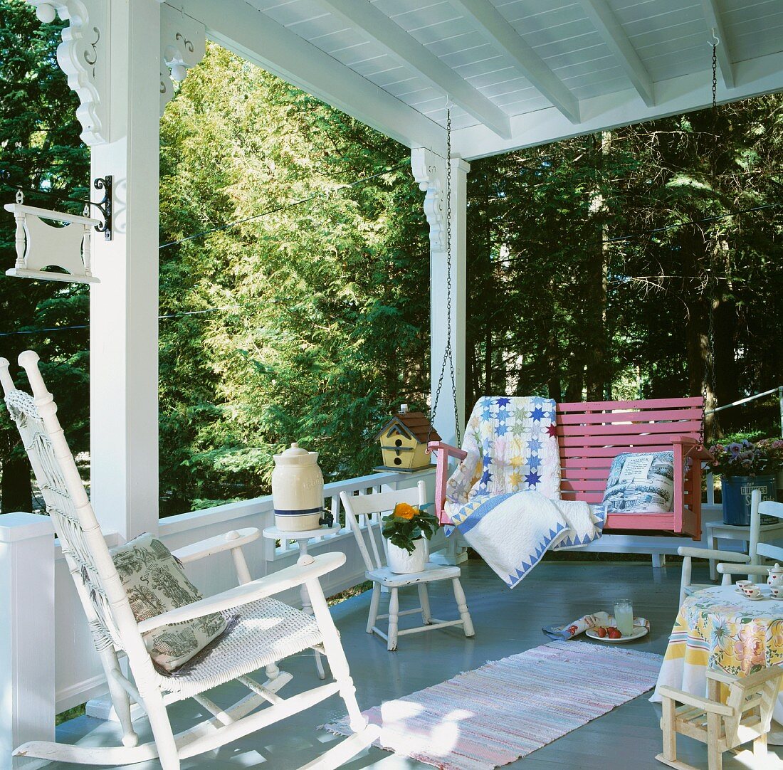 White wooden veranda in the country with white rocking chair, pink porch swing and children’s' chairs
