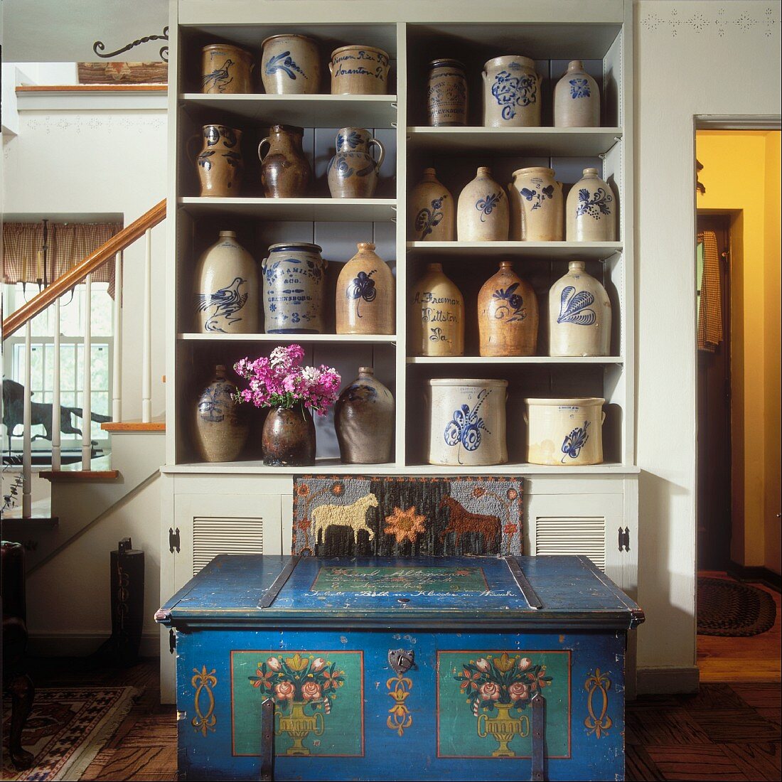 Shelving holding collection of 19th century stoneware with blue, hand-painted trunk in foreground