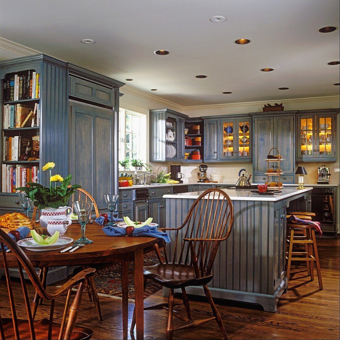 Open-plan kitchen with round dining table, wooden chairs and blue kitchen cupboards