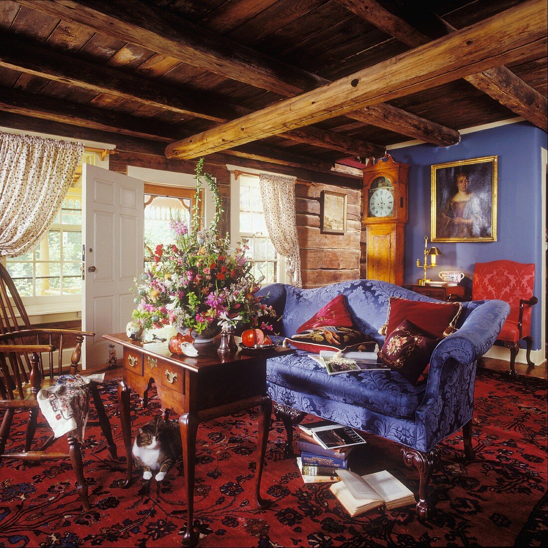 Wohnzimmer mit rustikaler Balkendecke, blauem Sofa, Lowboy-Tisch und Orientteppich