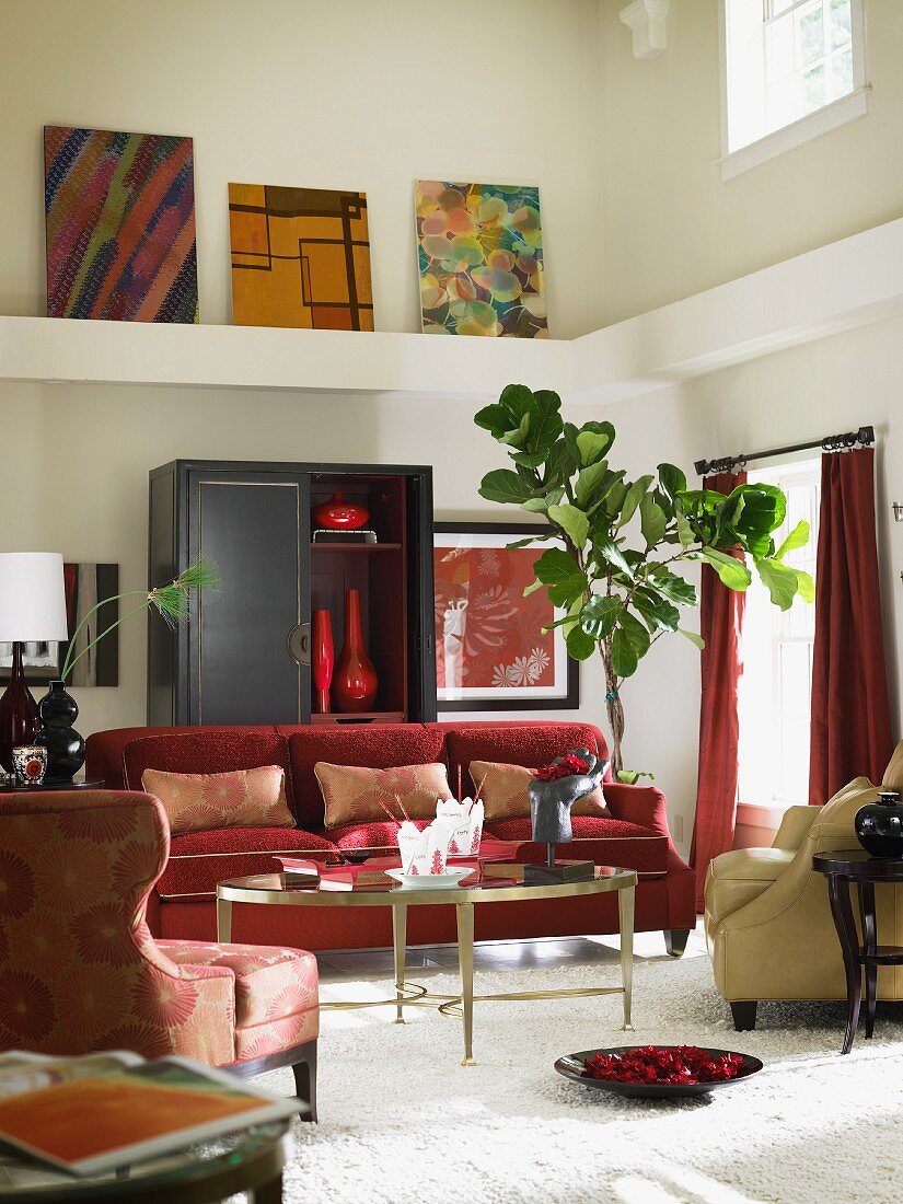 Wohnzimmer mit rotem Sofa vor einem schwarzem Schrank und moderne Malerei auf Sims im darüberliegenden Luftraum