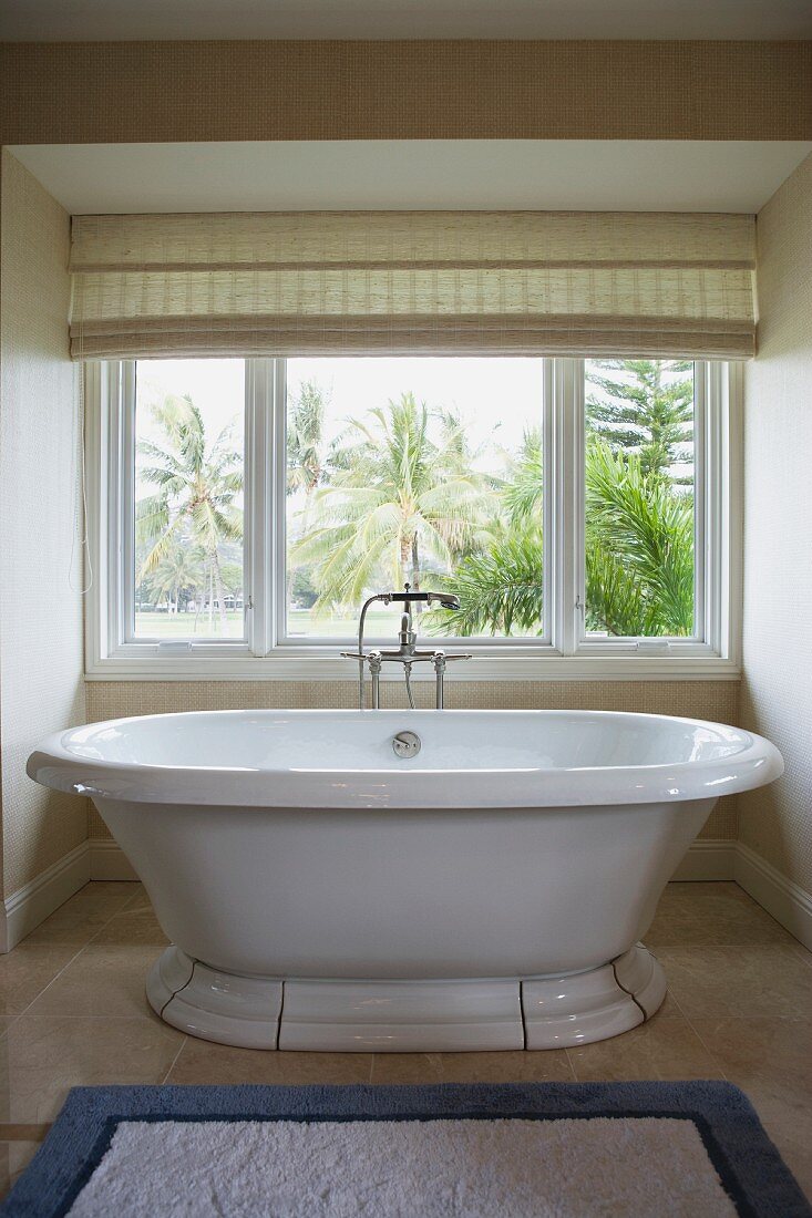 Modern bathtub with detachable shower head in front of window