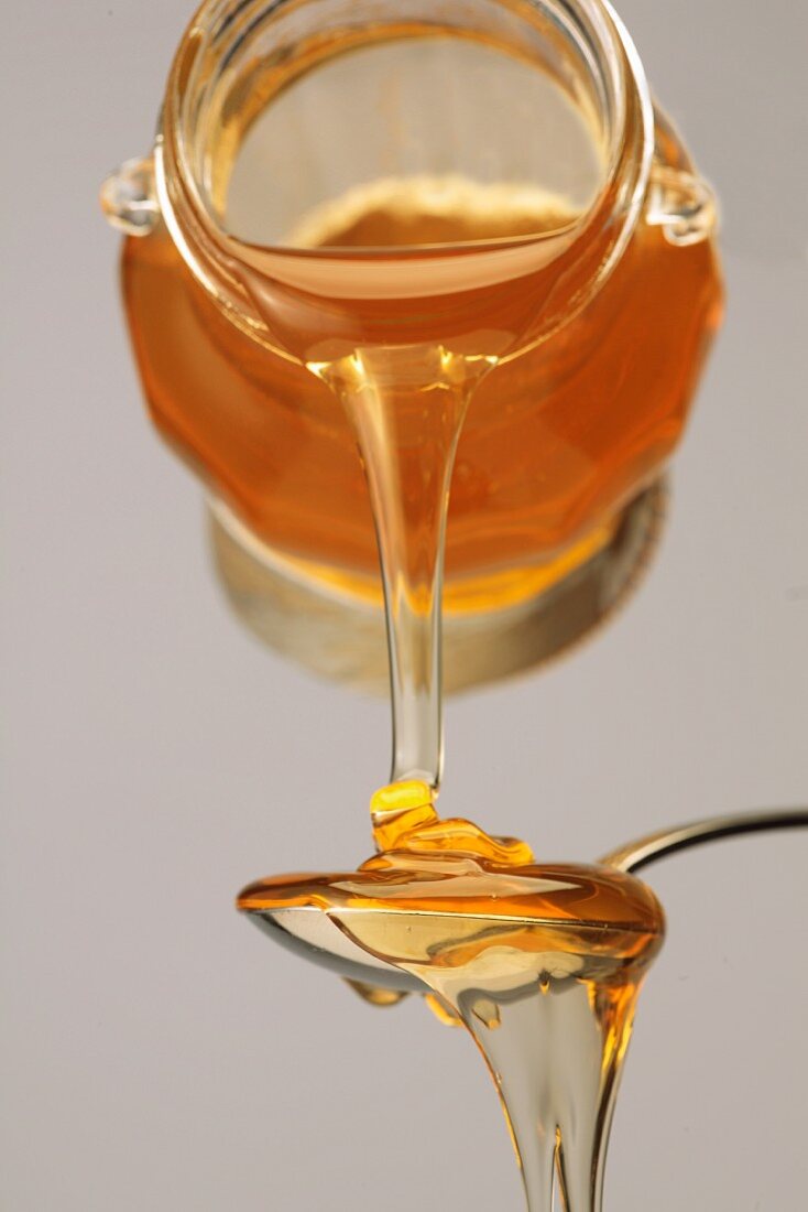 Honig fliesst aus dem Glas auf einen Löffel