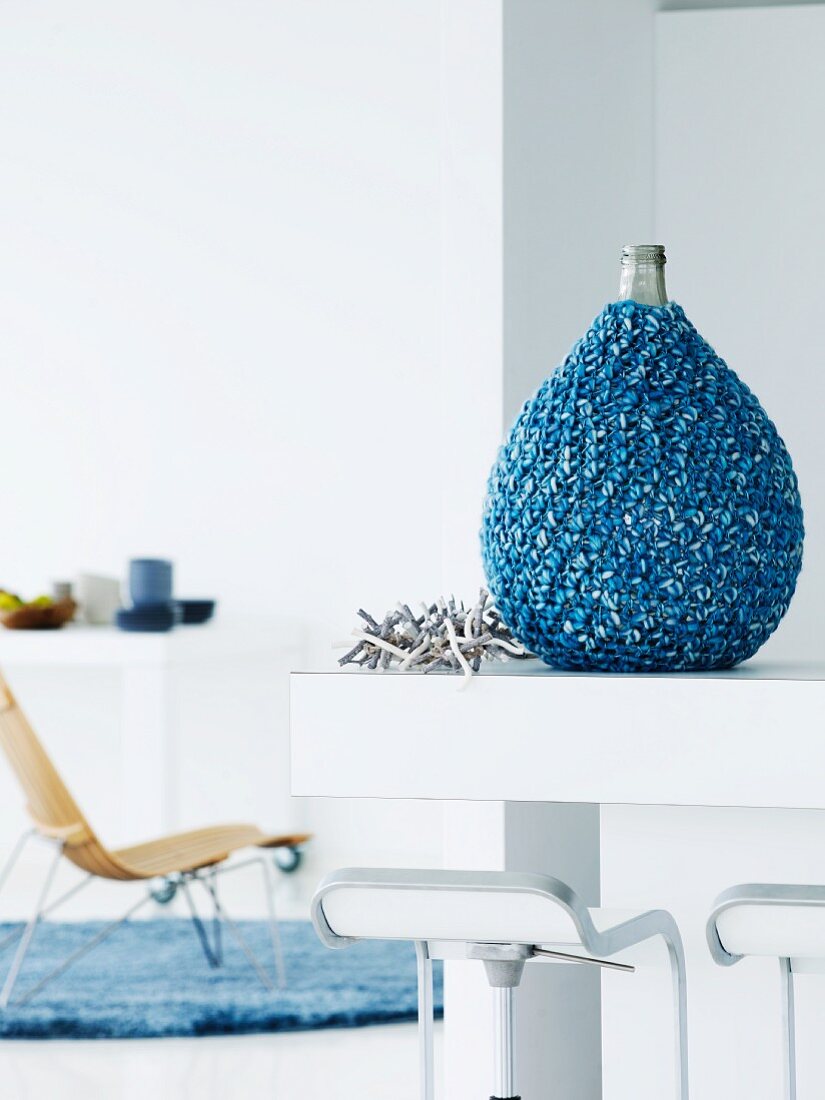 Pear-shaped bottle artistically encased in knitted, mottled blue yarn on kitchen counter