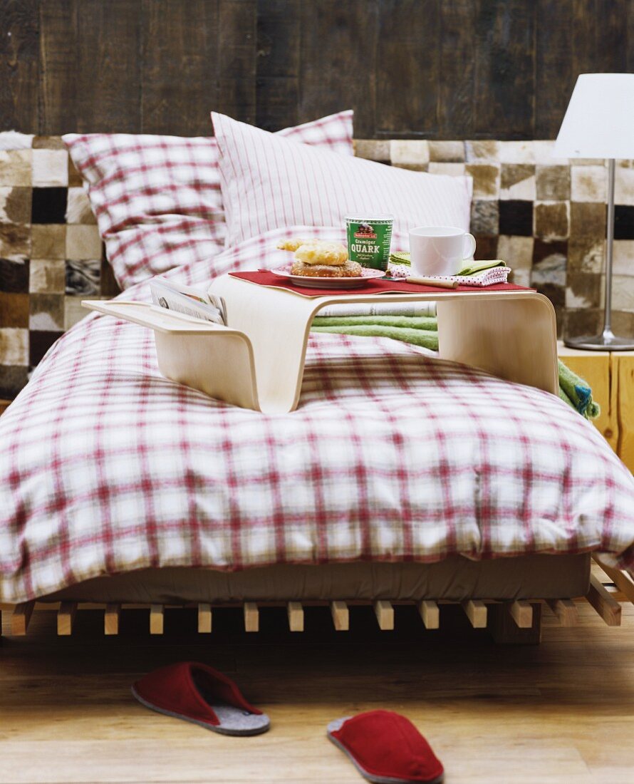 Bett mit kariertem Flanell-Bettwäsche vor Fell-Patchwork und Holzwand