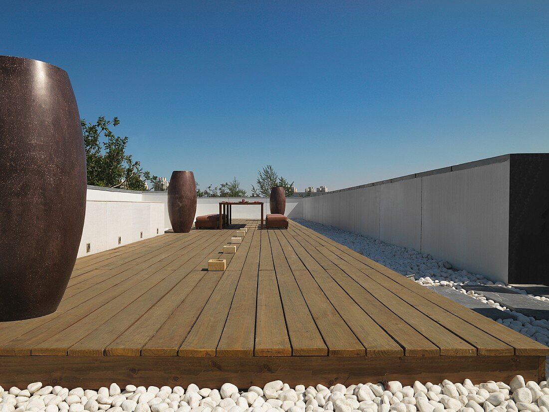 Dachterrasse mit dunkelbraunen Bodenvasen auf Holzdeck und Kieselsteinboden