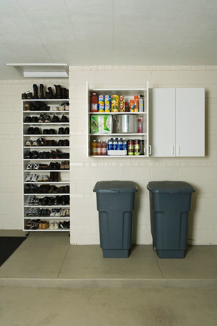 Grey plastic bins below open wall-mounted cupboard and shoe rack in utility room