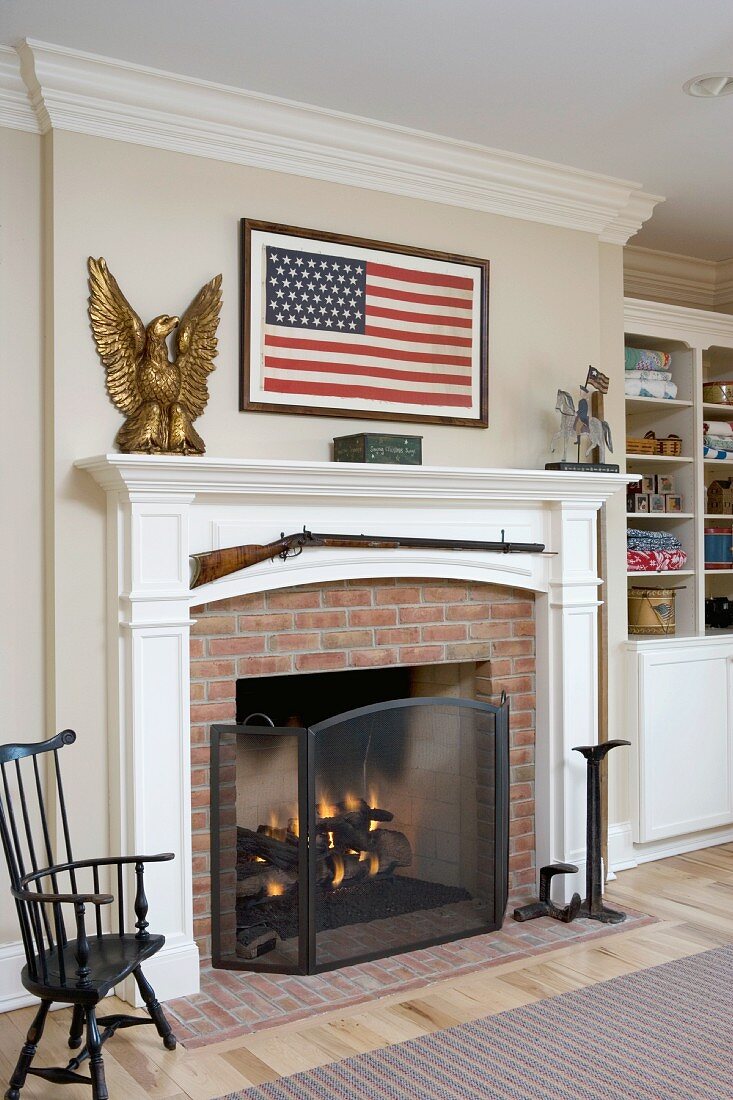 Kamin mit weiss lackiertem Holzsims und amerikanische Flagge an Wand im Wohnraum eines Landhauses