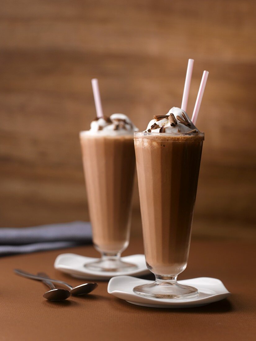Two Chocolate Milkshakes Topped with Whipped Cream and Chocolate Shavings; With Straws