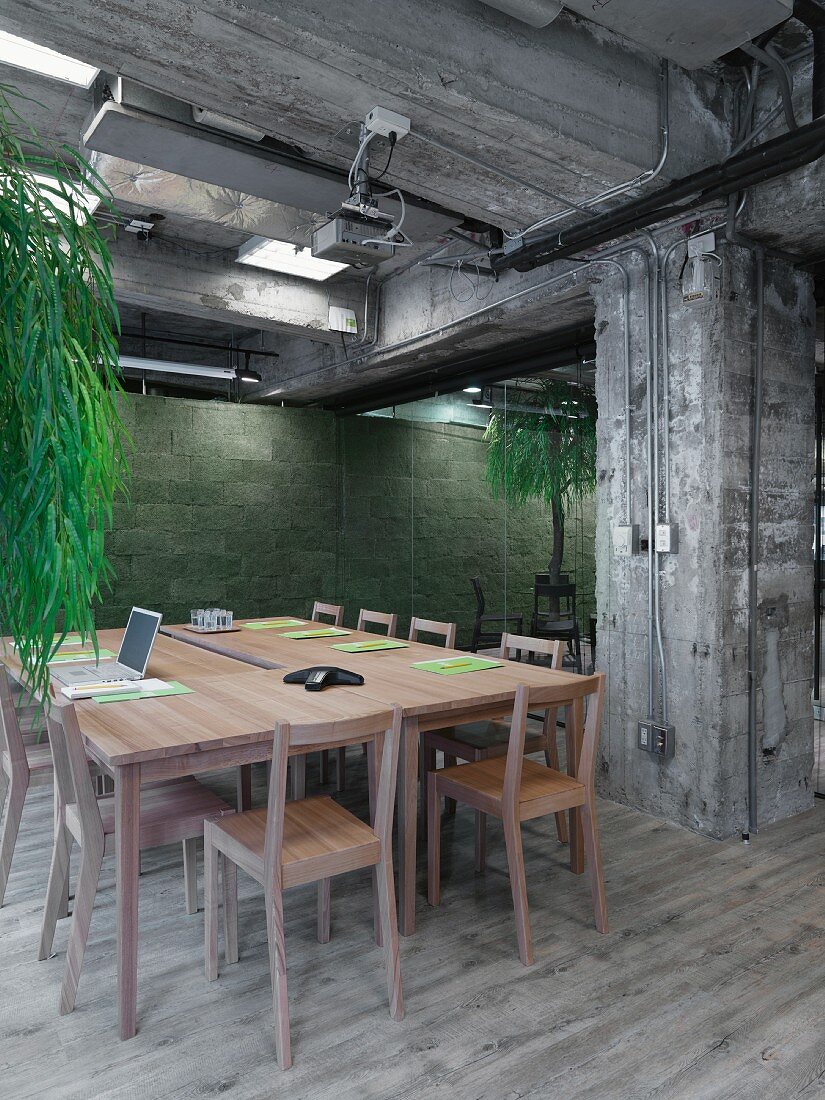 Konferenzraum in einem Loft mit Betonstützen, einem Konferenztisch aus hellem Holz und einem hellen Holzdielenboden