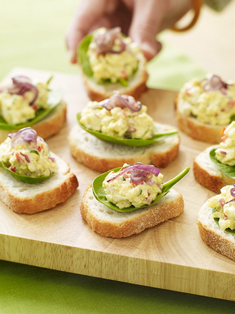 Slices of Bread Topped with Egg Salad on Baby Spinach Leaves