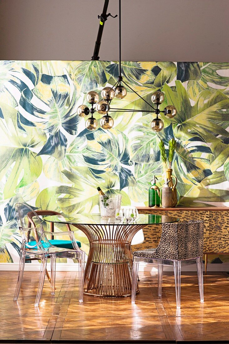Dining table with various chairs in front of a jungle wallpaper