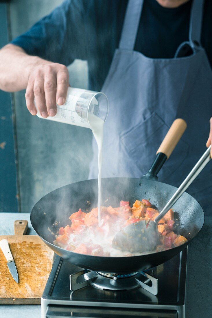 Sweet potatoes in a wok being quenched with coconut milk