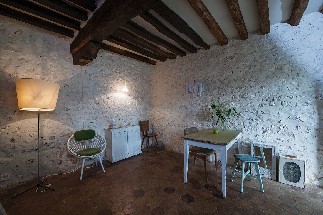 Kitchen table and wooden stools against white-painted stone wall below rustic wood-beamed ceiling