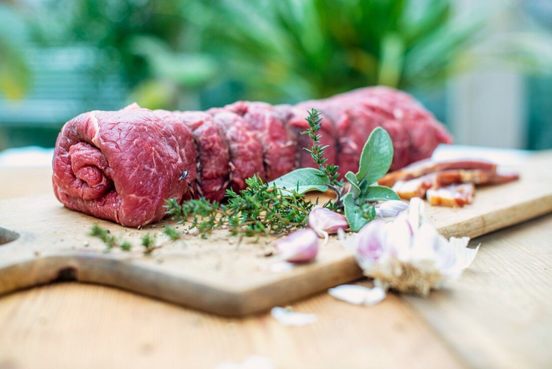 Ready-to-cook beef roulade with ingredients on a wooden chopping board