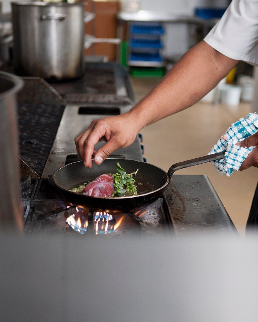 A chef frying lamb with wild herbs