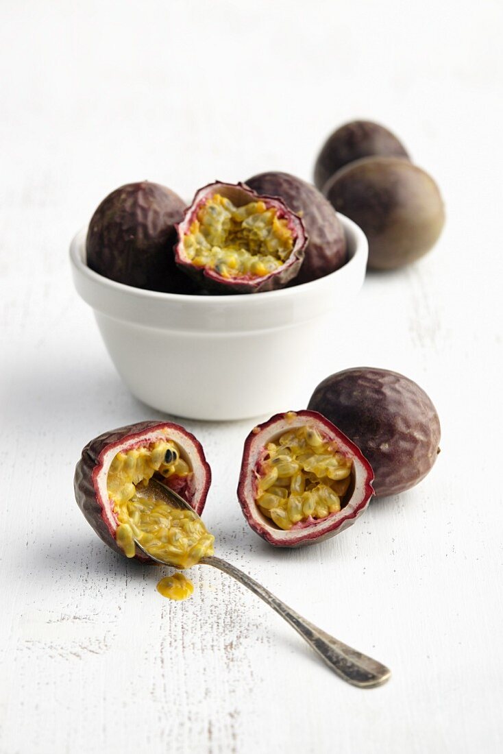 Passion fruit (whole and halved) being hollowed out with a spoon