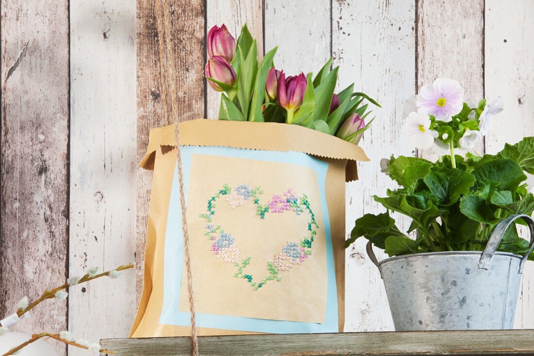 Vintage-style heart motif embroidered on paper bag and flowers on old wooden shelf