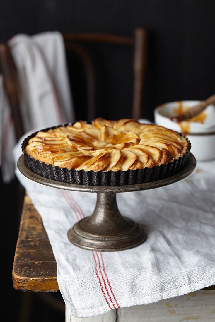 A whole apple and frangipane tart glazed with apricot jam on a cake stand