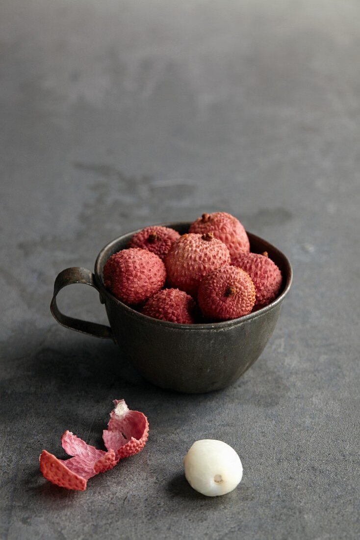 Lychees in a metal cup with a peeled lychee next to it