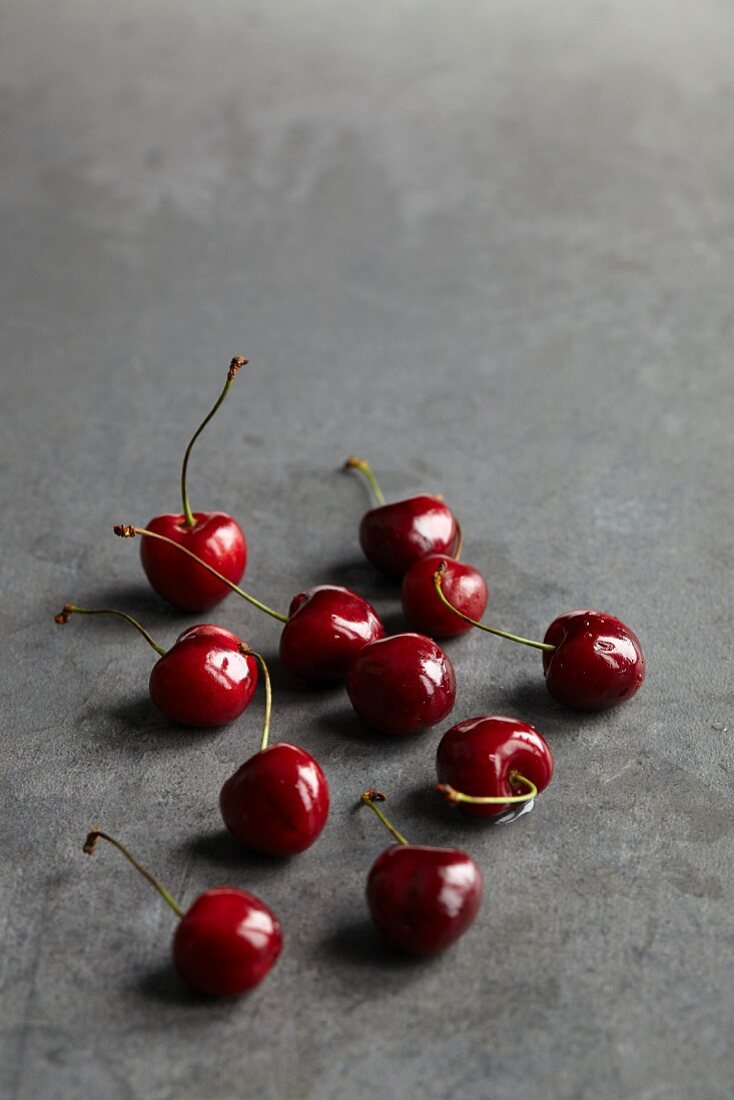 Red cherries scattered on a grey stone surface