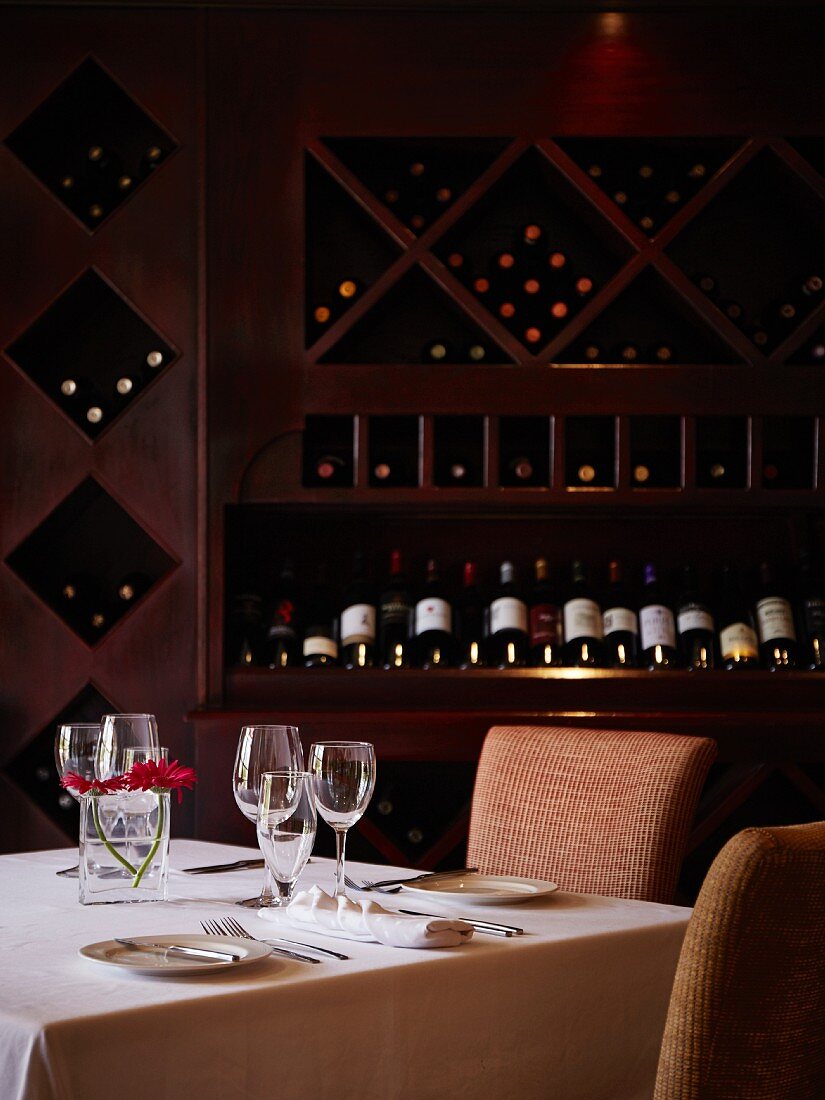 A table laid for two in front of a wine shelf in a restaurant
