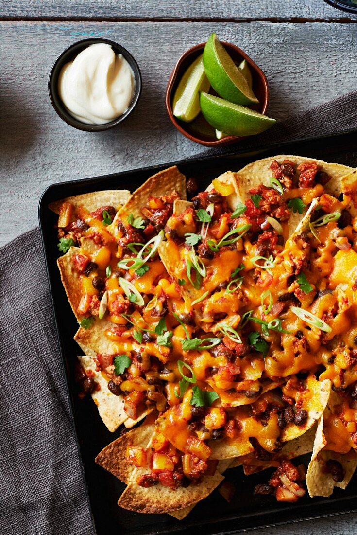 Chilli nachos topped with cheese on a baking tray