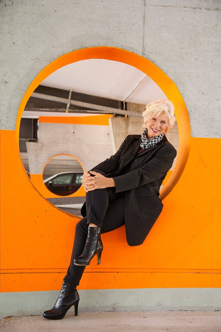 An older business woman sitting in a circle cut in a wall