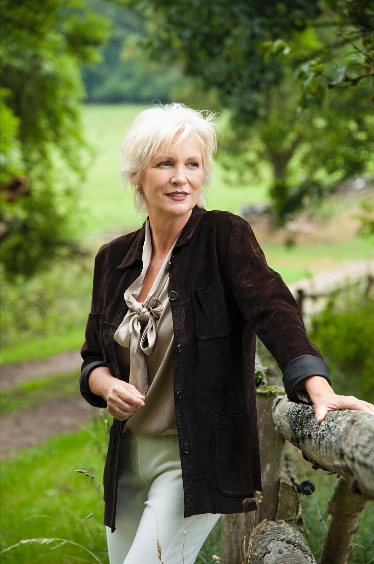 An older woman leaning on a wooden fence