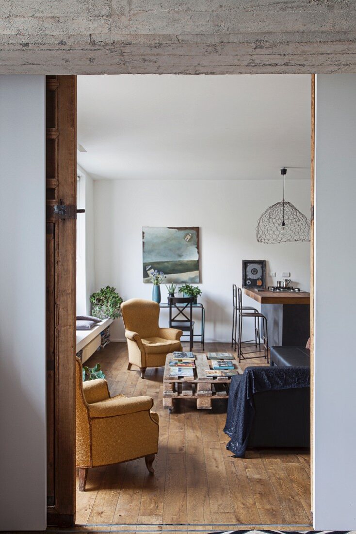 View of armchairs around pallet coffee table in living room with kitchen counter in background