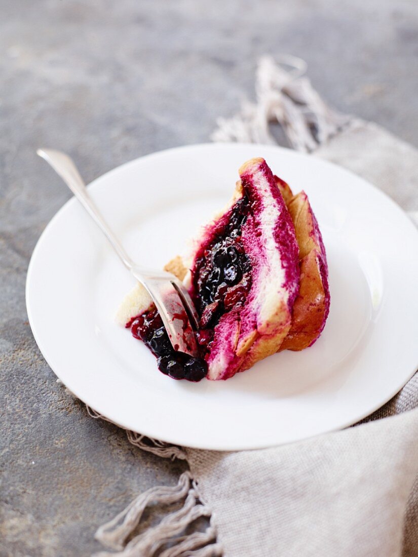 A slice of berry cake on a plate with a fork