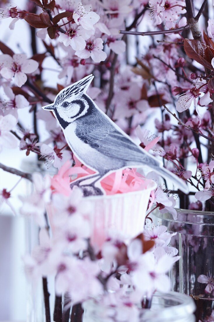 Papiervogel mit Nest aus Papierförmchen in Obstblütenstrauss