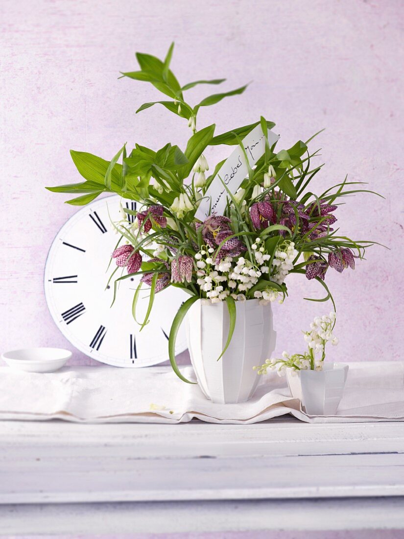 A bunch of spring flowers featuring lilly of the valley, chess flowers and Solomon's seal in front of a clock