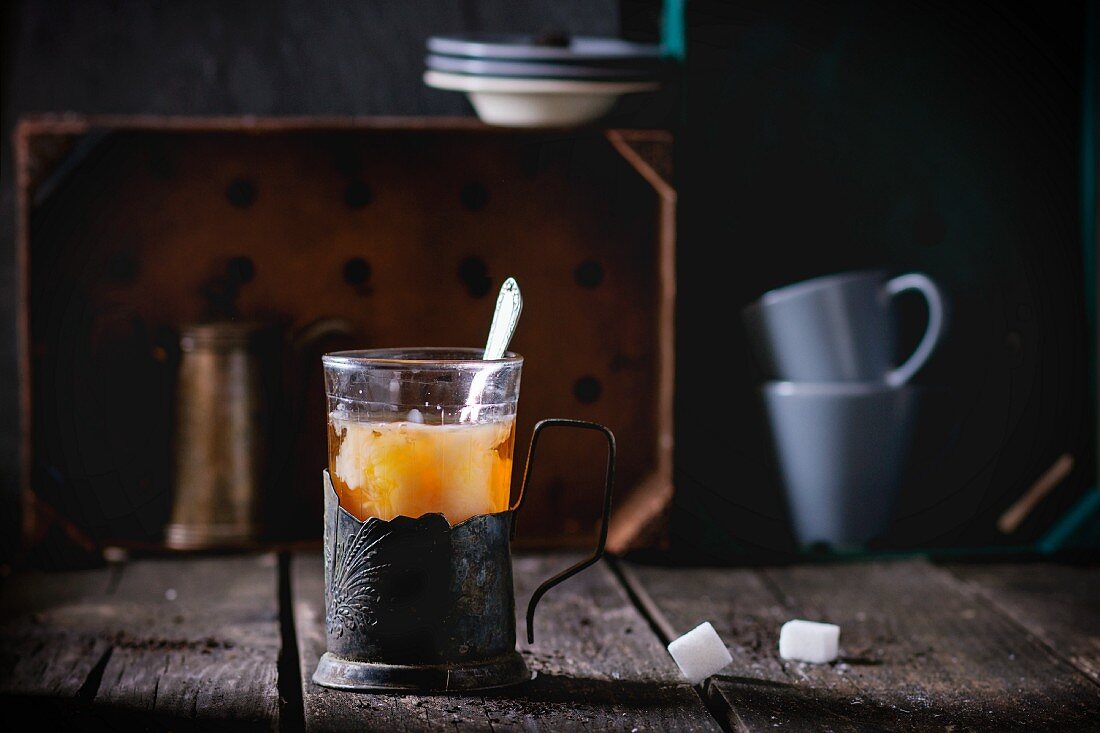 Tee mit Milch in Vintage-Teeglashalter auf rustikalem Holztisch