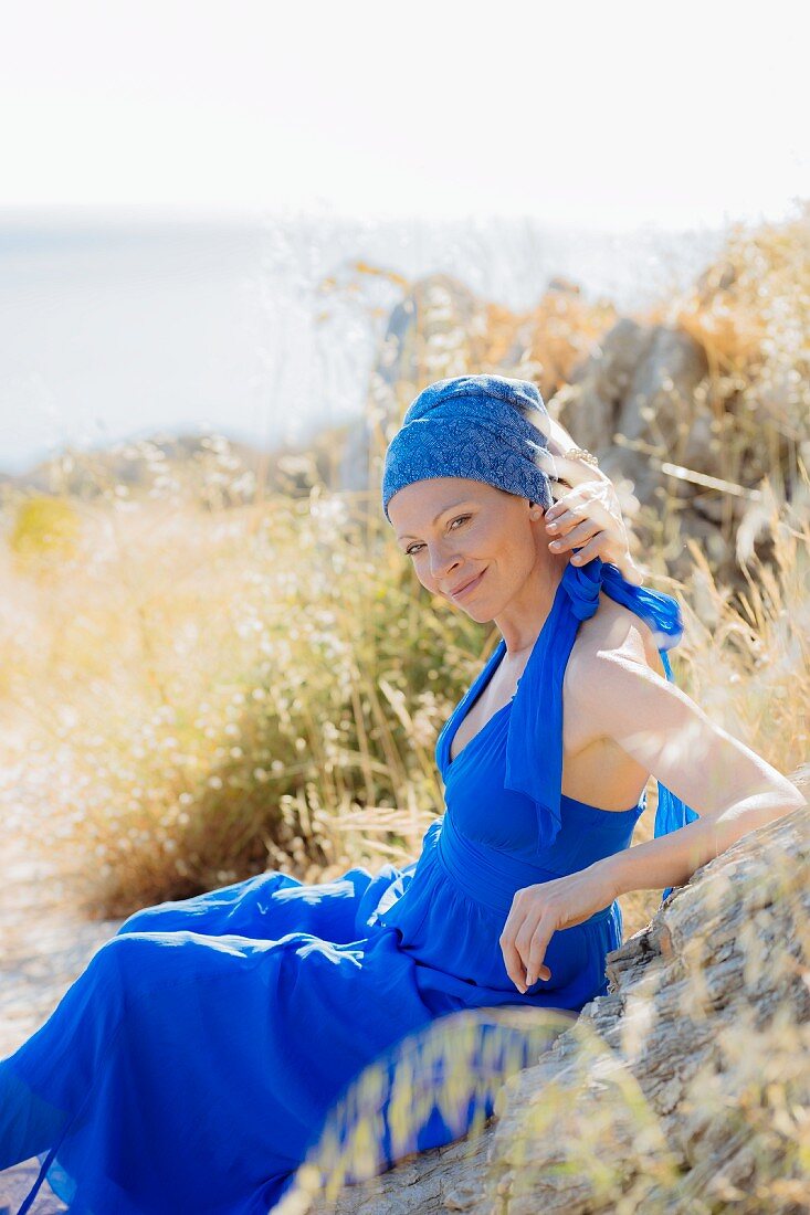 A woman wearing a blue dress and a turban sitting on a rock
