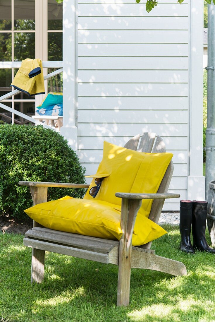 A wooden chair in a garden with a homemade cushion covers made from yellow raincoat material