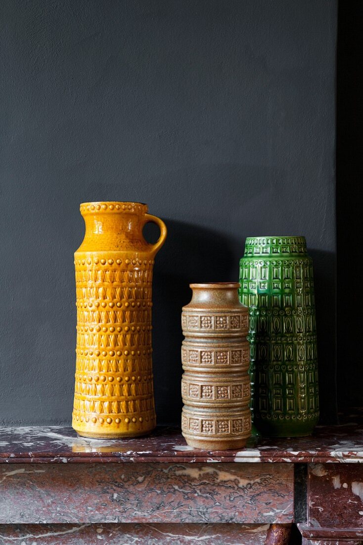 Collection of retro vases of various colours on mantelpiece against black wall