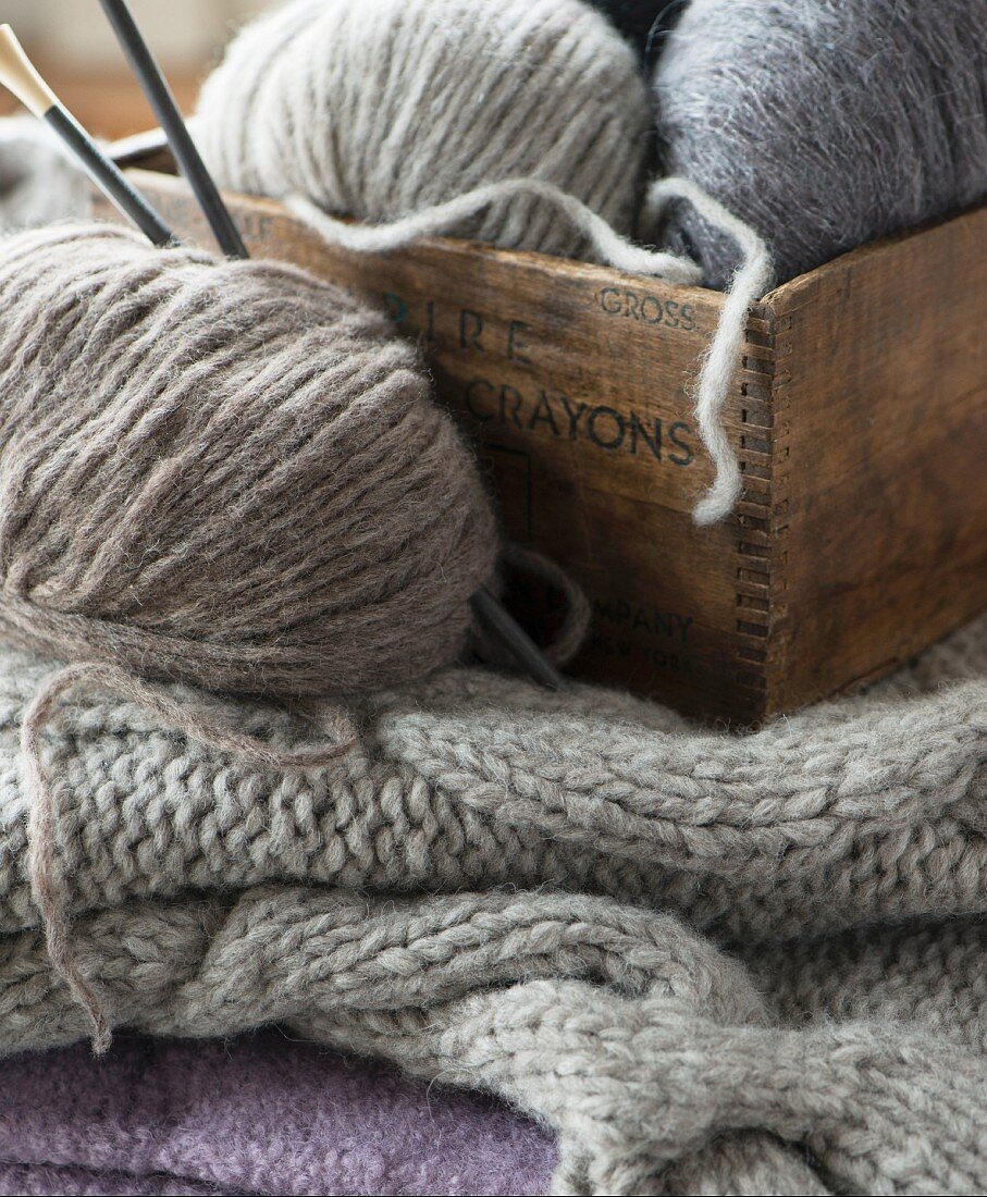 Knitting utensils and various boards of grey wool in a wooden crate