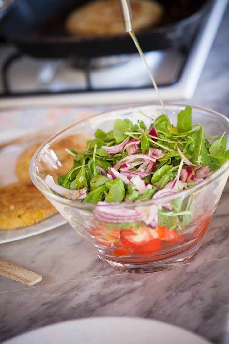 Green salad with red onions and tomatoes being drizzled with olive oil