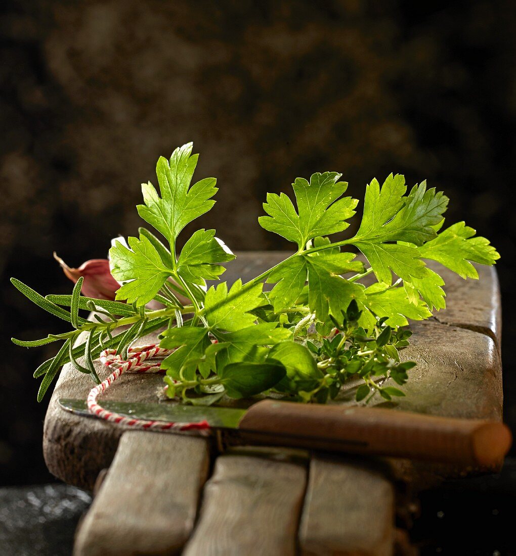 Flat leaf parsley, rosemary and other herbs on wooden board