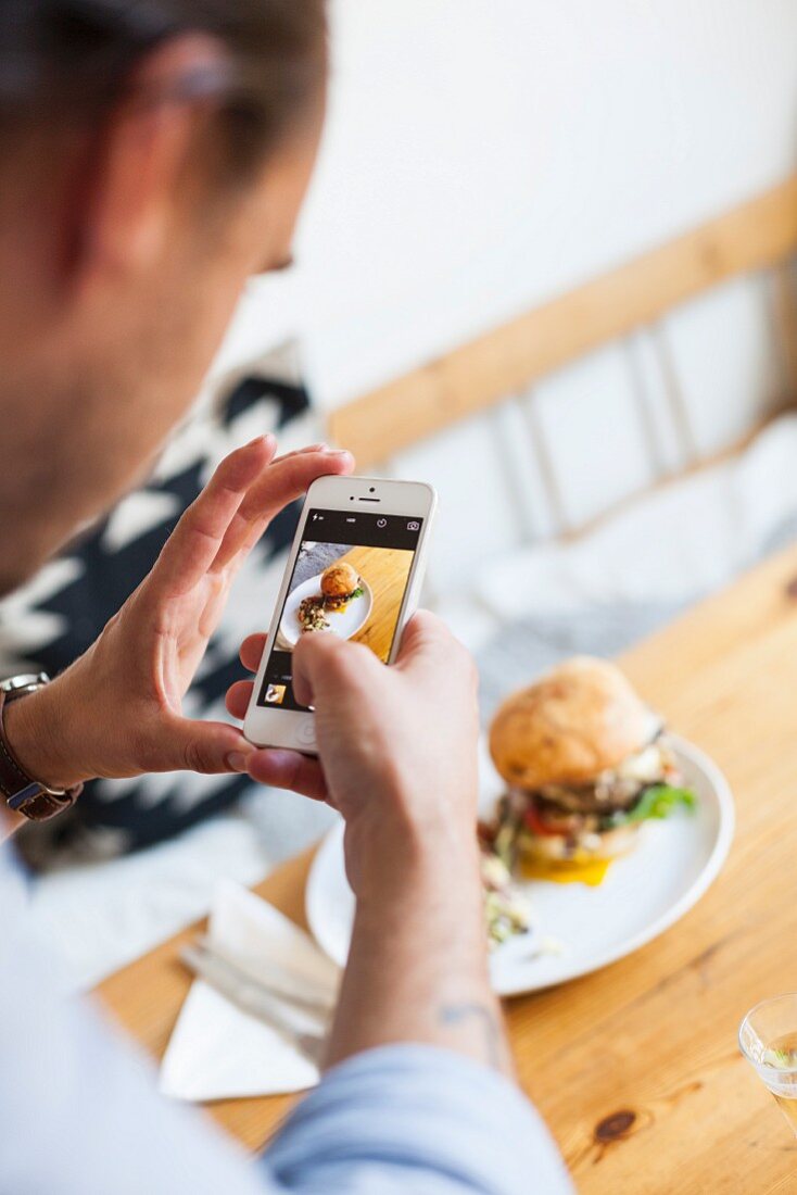 Mann fotografiert Burger mit Smartphone
