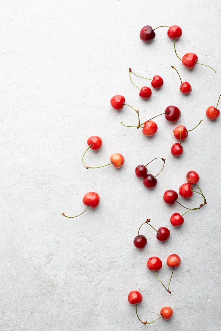 Fresh cherries on a white surface (seen from above)