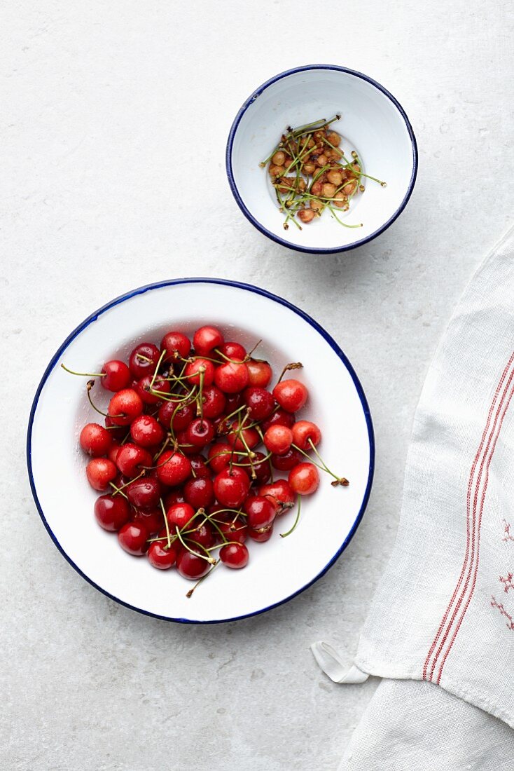 A bowl of cherries next to a bowl with stems and stones