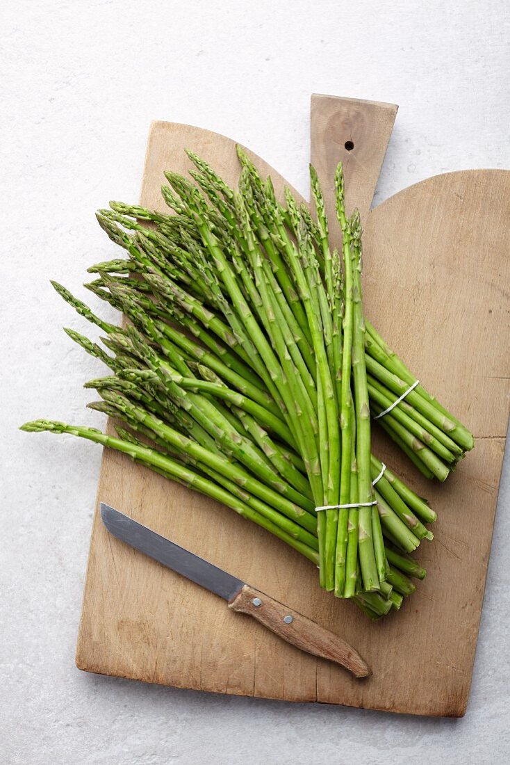 Bundles of green asparagus on a wooden chopping board (seen from above)
