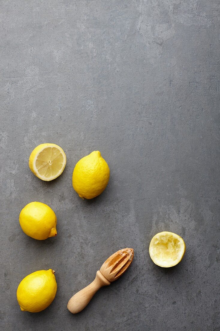 Lemons, whole and halved, with a wooden lemon squeezer (seen from above)