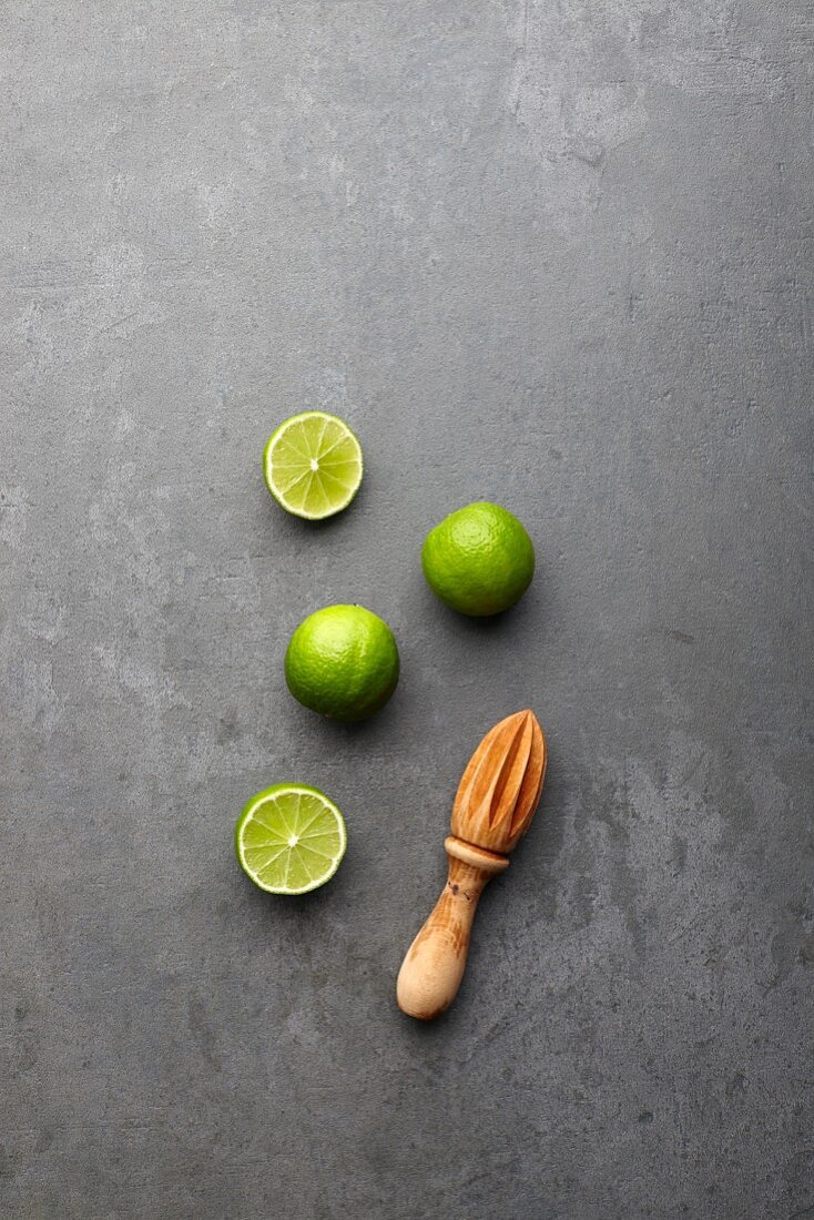 Limes, whole and halved, with a wooden juicer (seen from above)