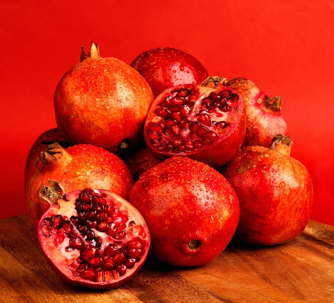 Granatäpfel und zwei Granatapfelhälften vor rotem Hintergrund
