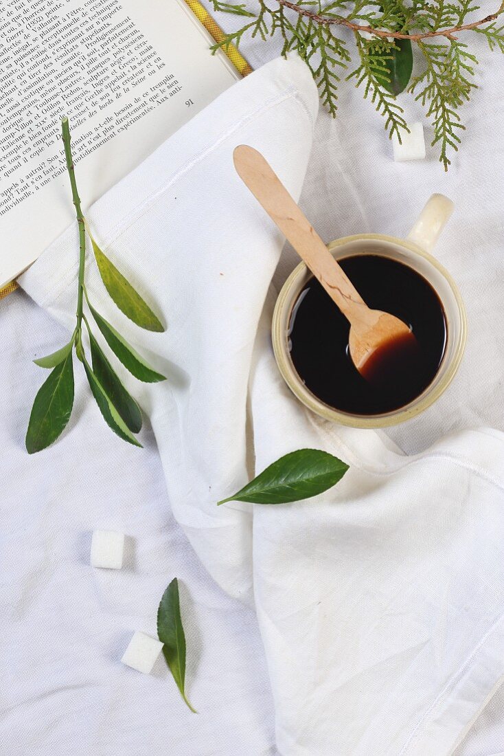 Schwarzer Kaffee in Tasse mit Holzlöffel, daneben Zuckerwürfel und Blätter